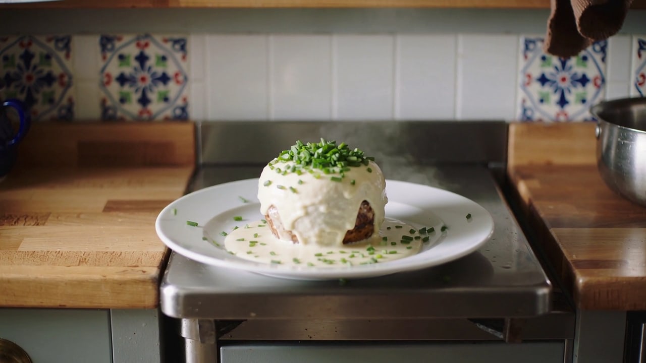 Teller mit einem runden Fleischgericht unter Rahmsauce und Schnittlauch auf einer Edelstahlablage, Küche des erfundenen Restaurants Silberpfanne
